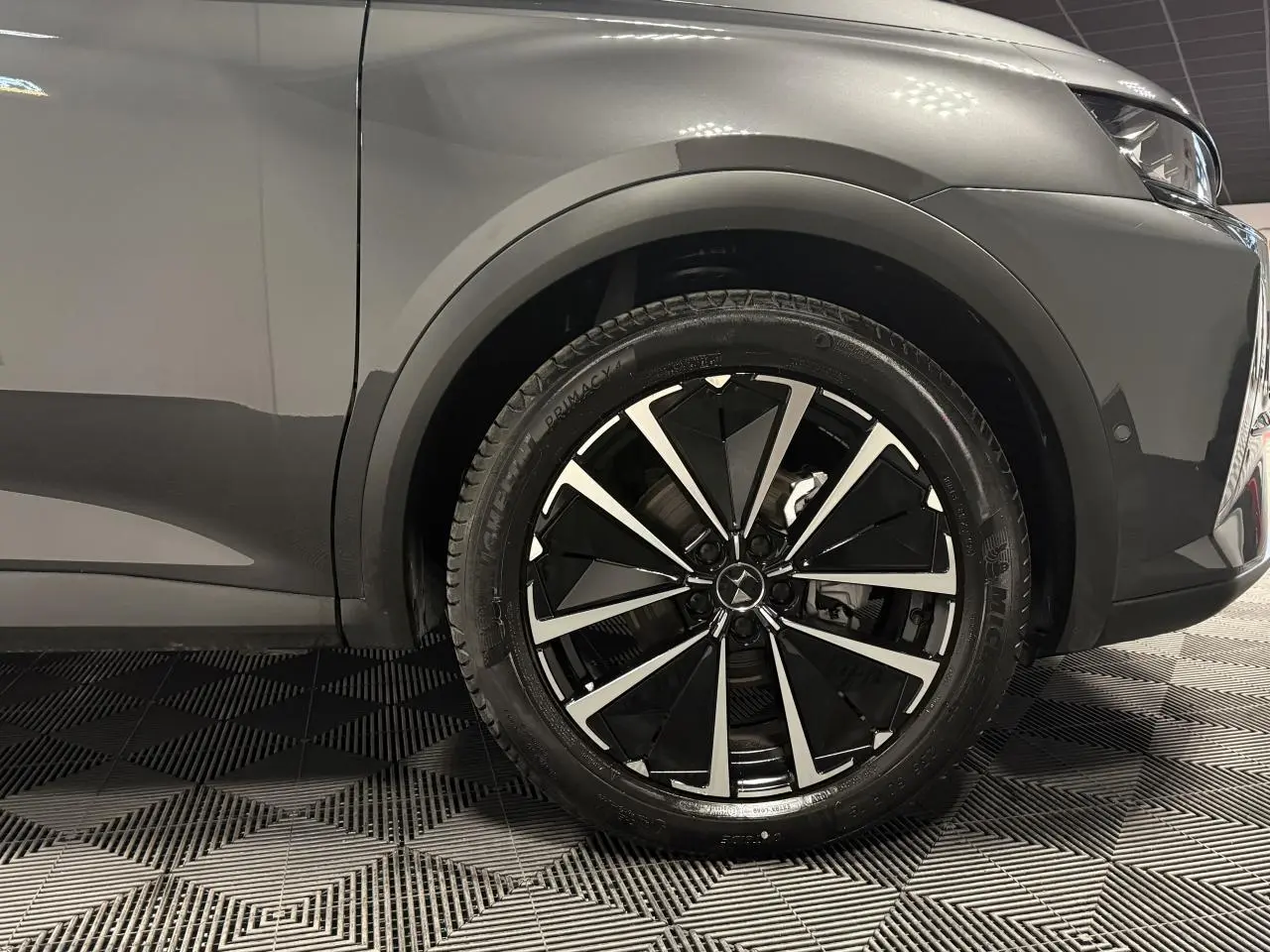 Gros plan sur la roue avant droite du DS7 Crossback gris, avec jante alliage noire et argentée au design moderne.