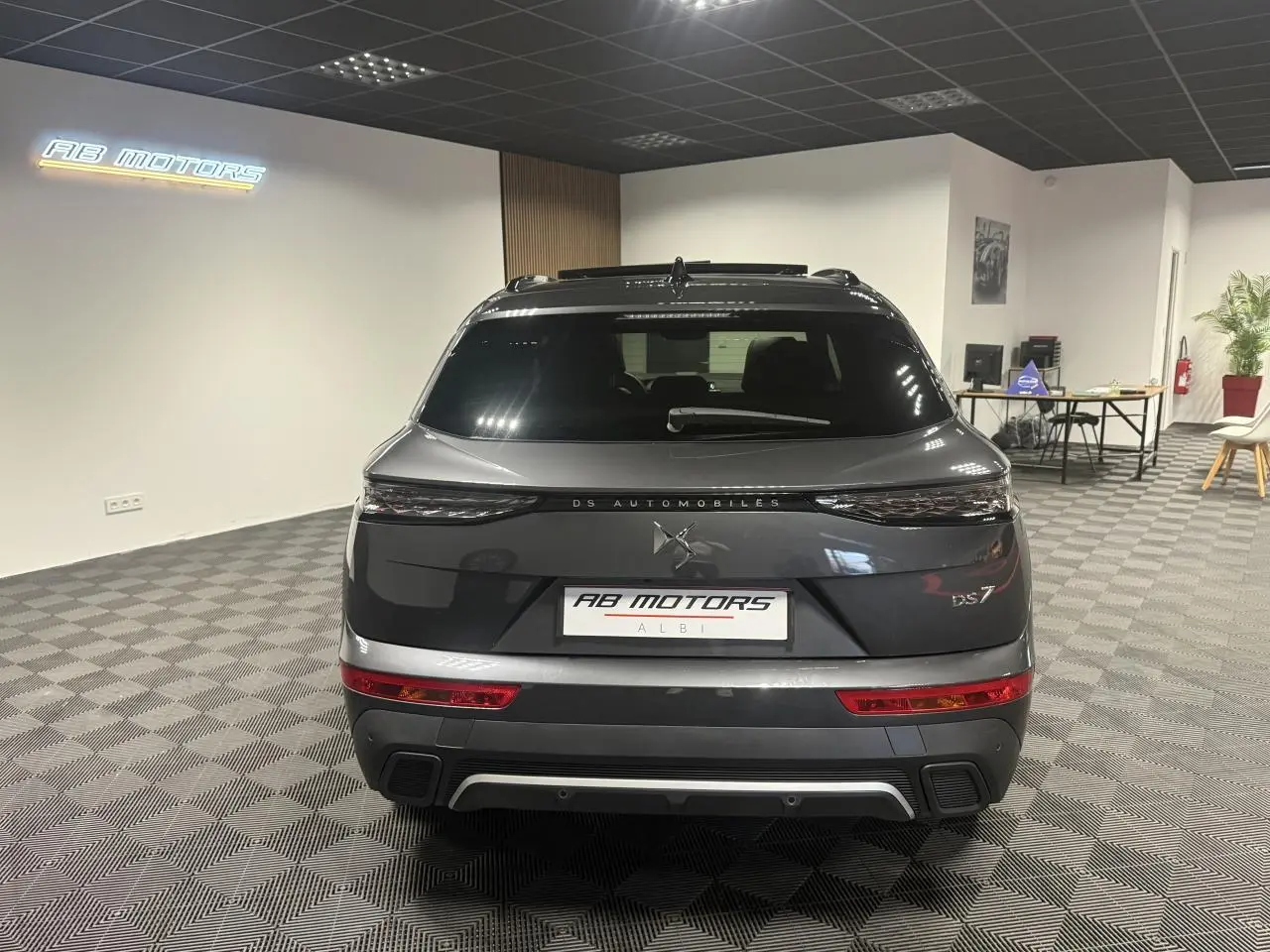 Vue arrière du DS7 Crossback gris métallisé 2025 avec feux arrière 3D et logo DS Automobiles visible en showroom.