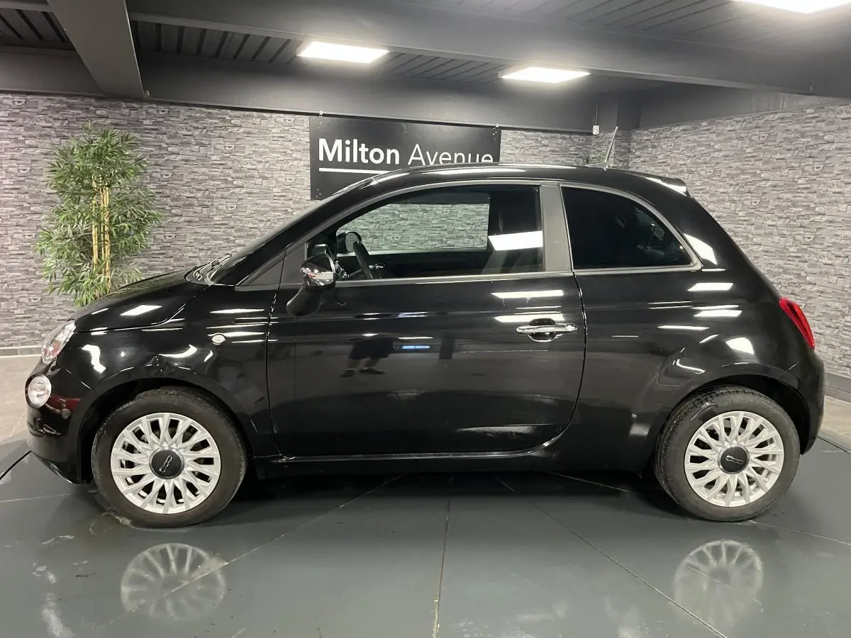 Profil côté gauche d'une Fiat 500 noire 2023 avec jantes alliage et poignées chromées dans un showroom.