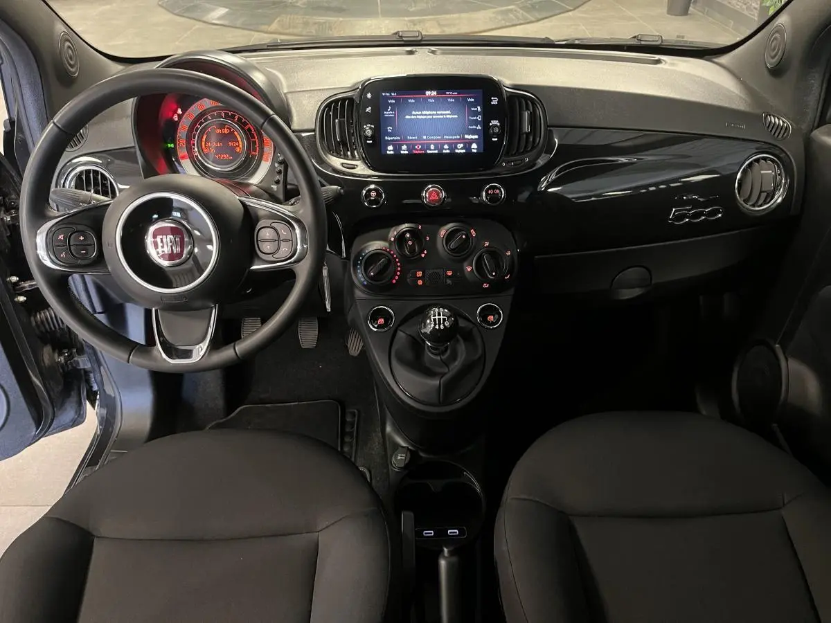 Tableau de bord noir de la Fiat 500 2023 vue de face, avec volant multifonction et écran tactile central.