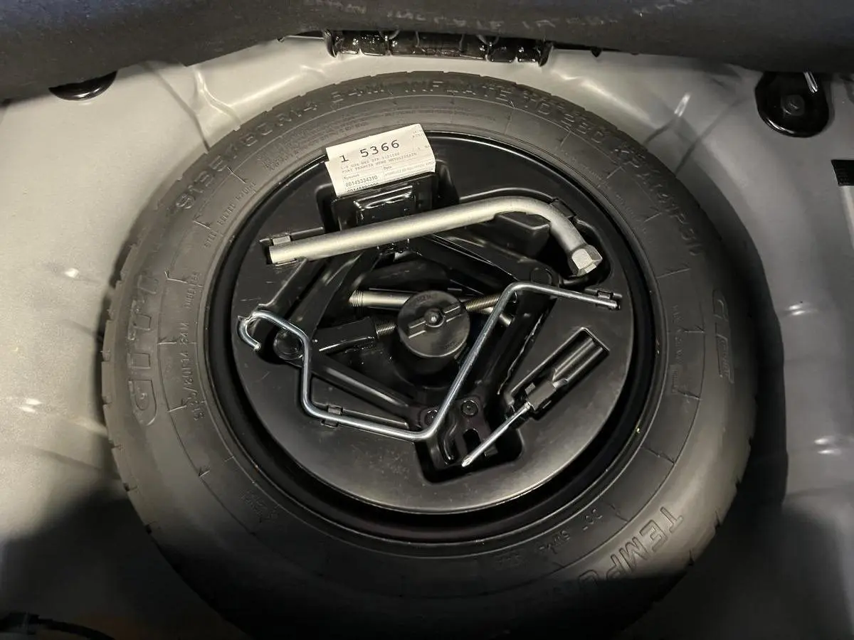 Gros plan sur la roue de secours noire et ses outils dans le coffre de la Fiat 500 Dolcevita noire 2023.