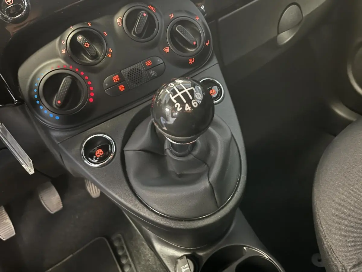 Gros plan sur le levier de vitesses manuel noir et les commandes de climatisation d'une Fiat 500 noire 2023.
