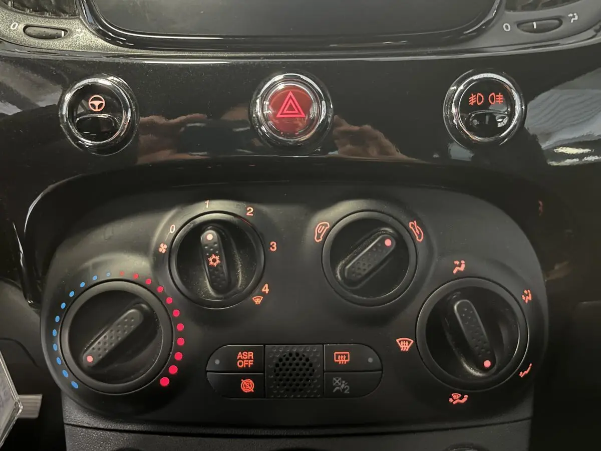 Commandes de climatisation et boutons de sécurité en gros plan sur la planche de bord noire de la Fiat 500 Dolcevita 2023.