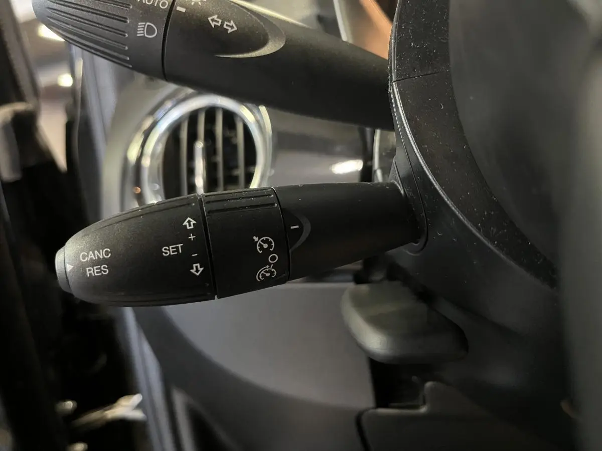 Gros plan sur la commande de régulateur de vitesse noire, avec volant et aérateur chromé d'une Fiat 500 noire 2023.