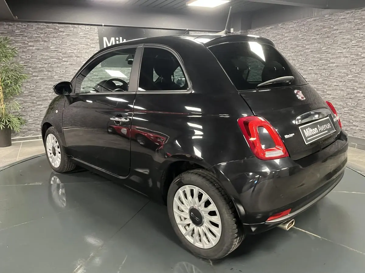 Fiat 500 noire vue en 3/4 arrière droit, avec jantes alliage et feux arrière distinctifs dans un showroom.