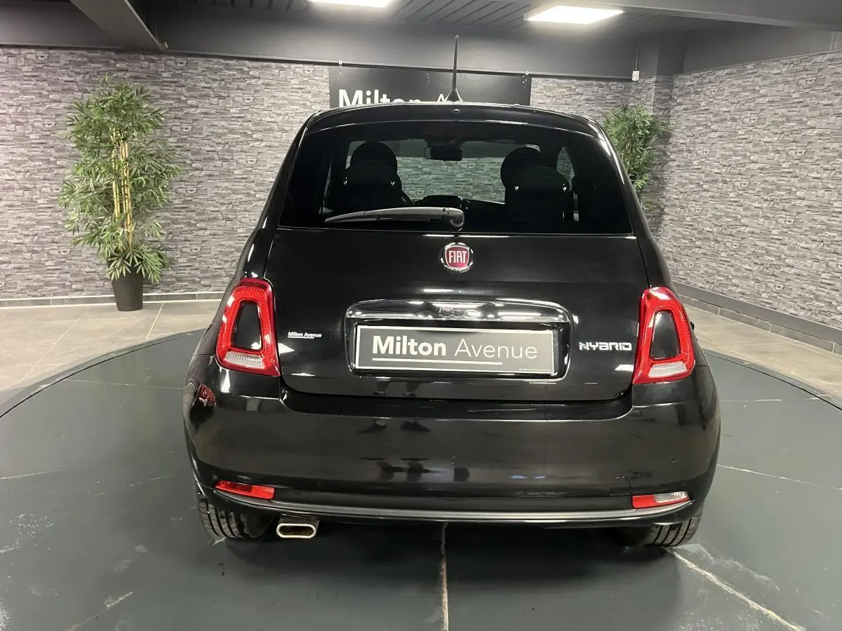 Vue arrière d'une Fiat 500 noire hybride 2023 avec logo FIAT et plaque Milton Avenue dans un showroom.
