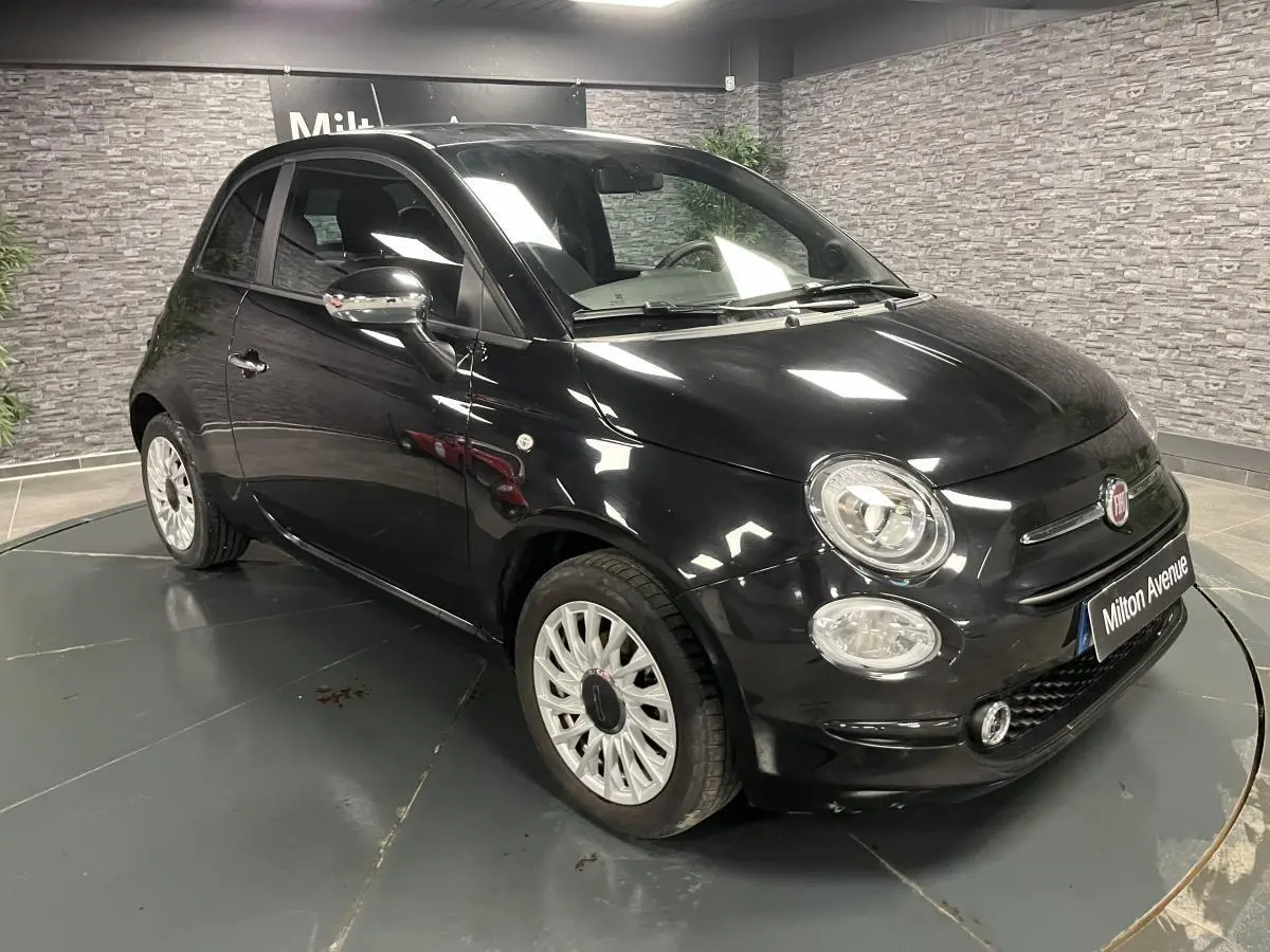 Fiat 500 noire vue en 3/4 avant droit, avec jantes alliage blanches et rétroviseurs chromés dans un showroom.