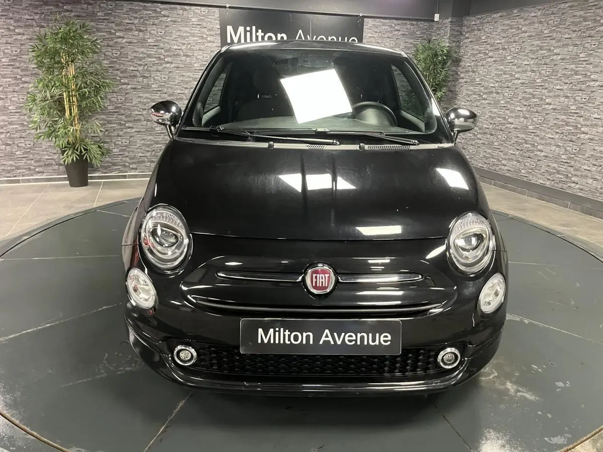 Vue frontale d'une Fiat 500 noire avec calandre chromée et projecteurs ronds dans un showroom.