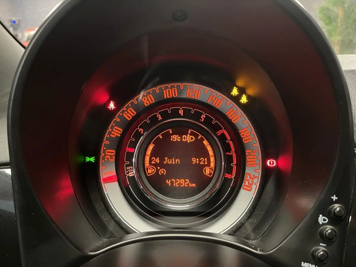 Vue rapprochée du tableau de bord numérique orange de la Fiat 500 noire avec affichage du compteur et témoins allumés.
