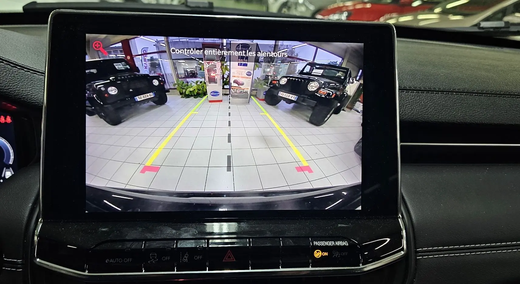 Vue arrière via caméra de recul du Jeep Compass noir dans un showroom avec deux autres Jeep noires visibles de chaque côté.