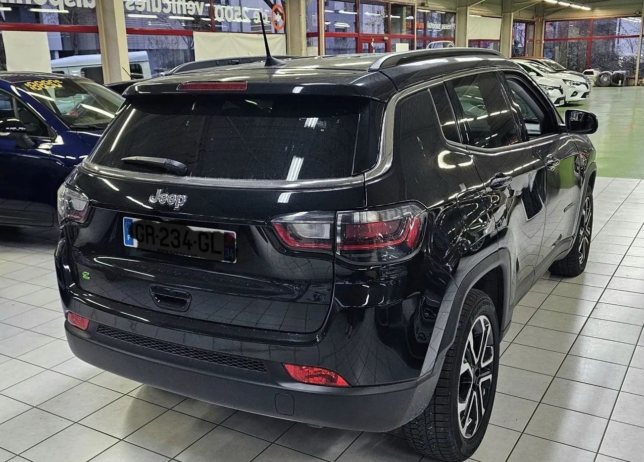 Vue 3/4 arrière droite d'un Jeep Compass noir 2023 en intérieur, avec feux arrière et jantes visibles.