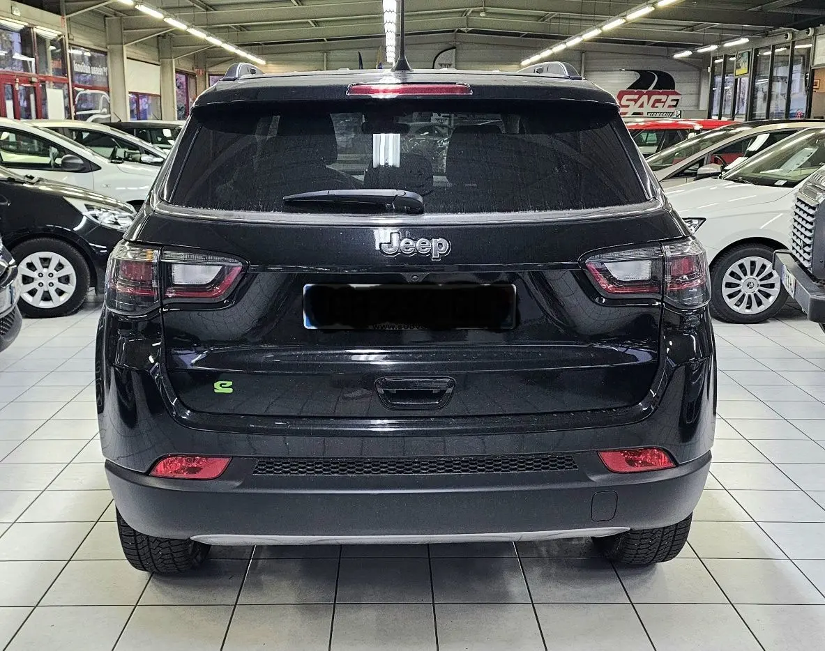 Vue arrière du Jeep Compass noir 2023 avec logo vert hybride, feux arrière et lunette teintée en intérieur showroom.