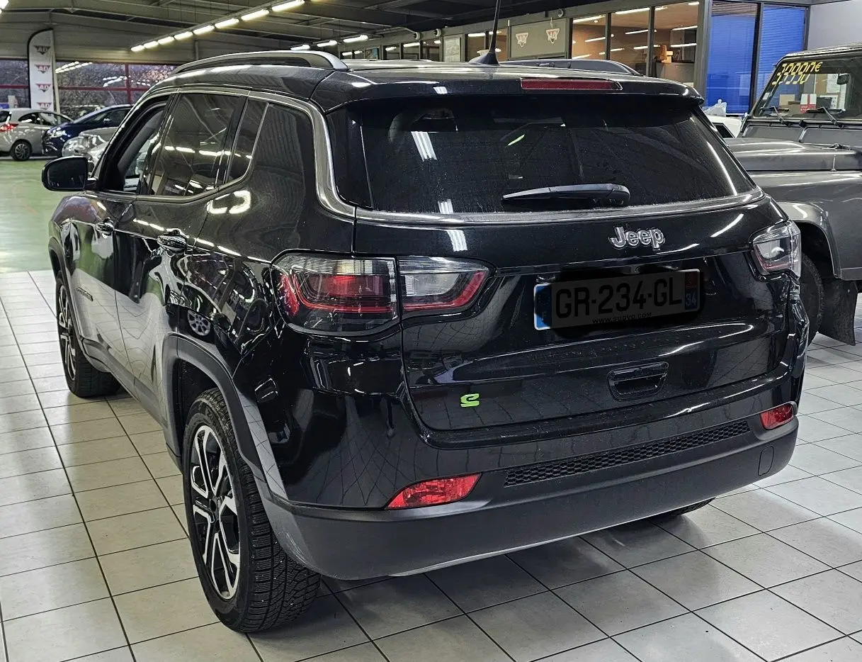 Vue 3/4 arrière d'un Jeep Compass noir brillant en hybride essence, avec jantes alliage et feux arrière LED visibles.