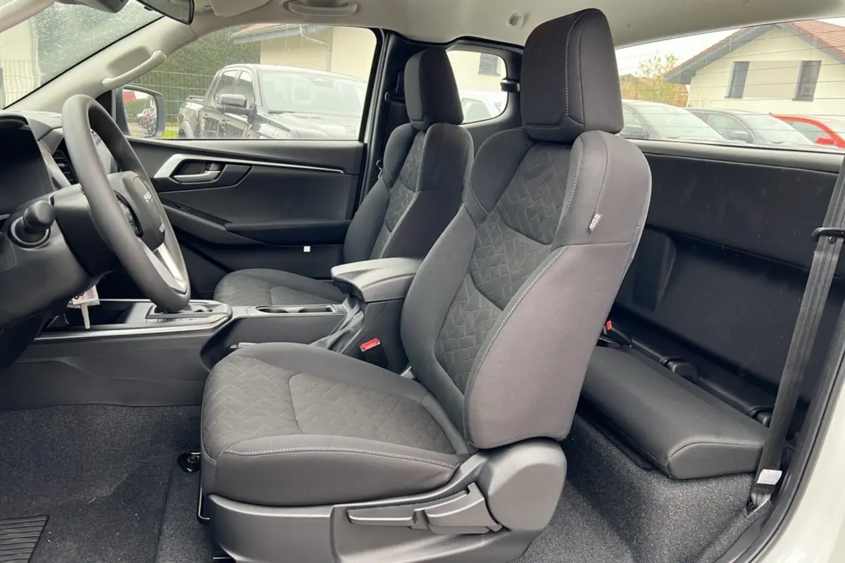 Vue intérieure côté gauche du pickup Isuzu D-MAX 2026 Splash White, montrant les sièges avant en tissu noir et l'accoudoir central.