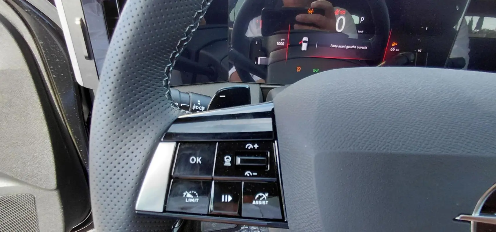 Gros plan sur le volant perforé et les commandes multifonctions de l’Opel Astra noire, avec tableau de bord numérique en arrière-plan.