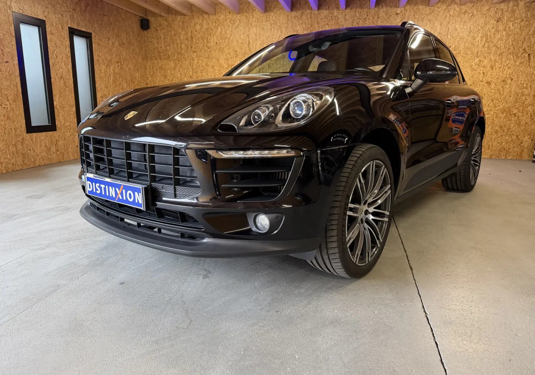Vue 3/4 avant droite d’un Porsche Macan S noir brillant avec jantes alu 21 pouces et phares bi-xénon en intérieur bois.