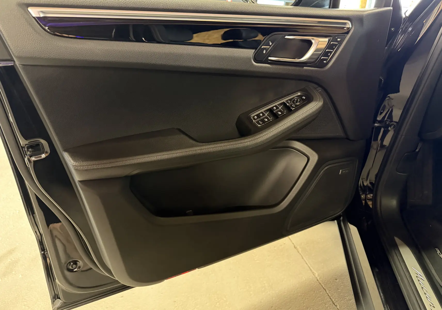 Vue rapprochée de la porte avant gauche noire du Porsche Macan S avec commandes électriques et finition intérieure noire.