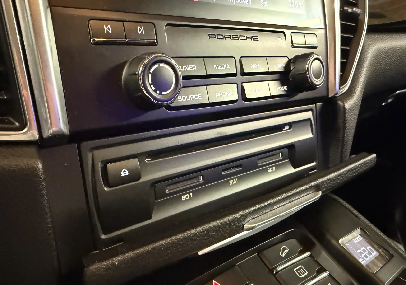 Gros plan sur la console centrale noire d’un Porsche Macan S, mettant en valeur les commandes multimédia et les ports SD.
