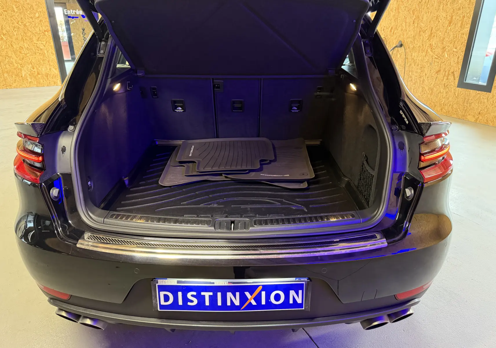 Coffre ouvert vu de l'arrière d'un Porsche Macan S noir avec tapis de sol Porsche et feux arrière LED visibles.