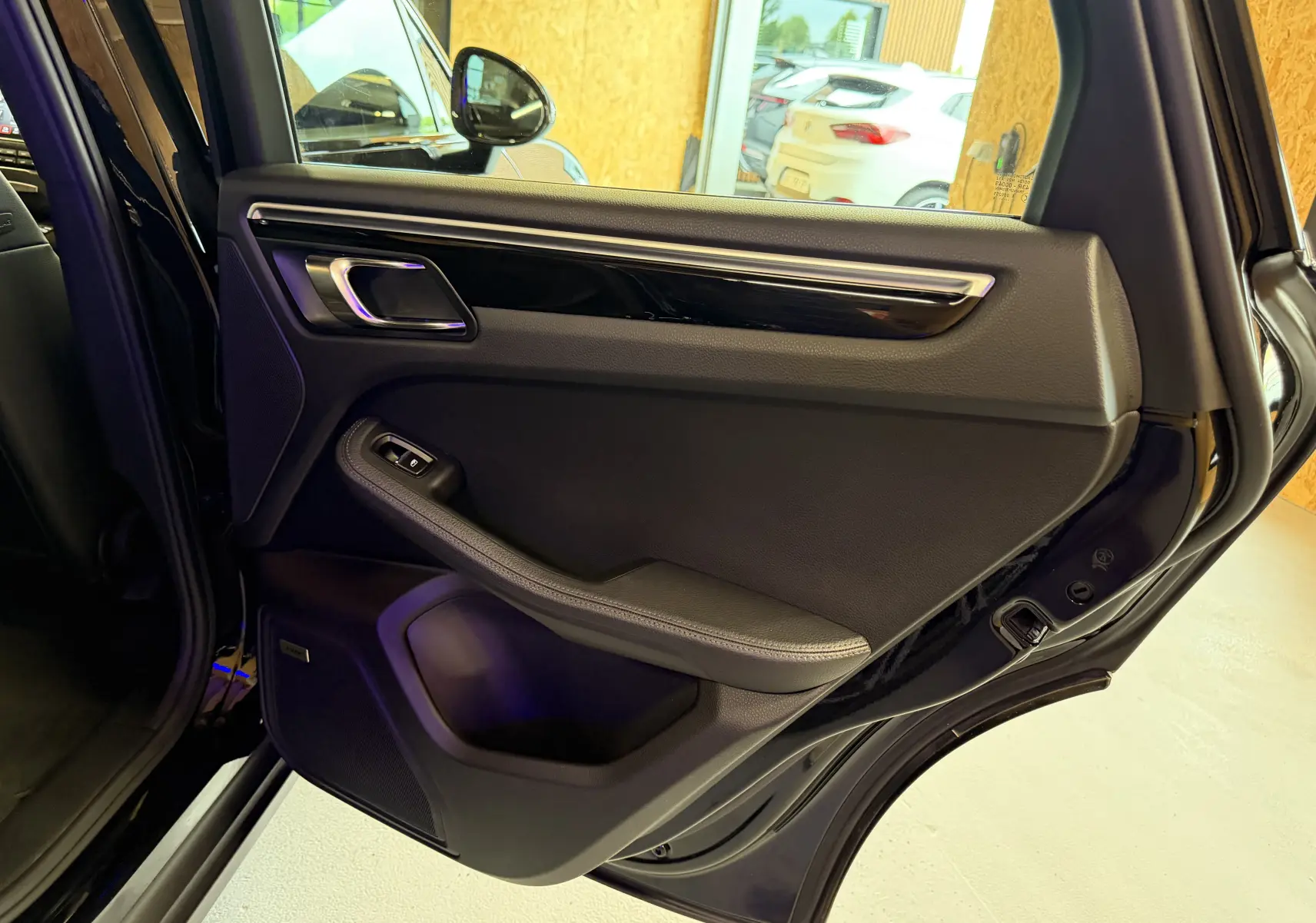 Vue intérieure de la porte arrière gauche noire du Porsche Macan S 3.0i avec garniture cuir et insert décoratif brillant.