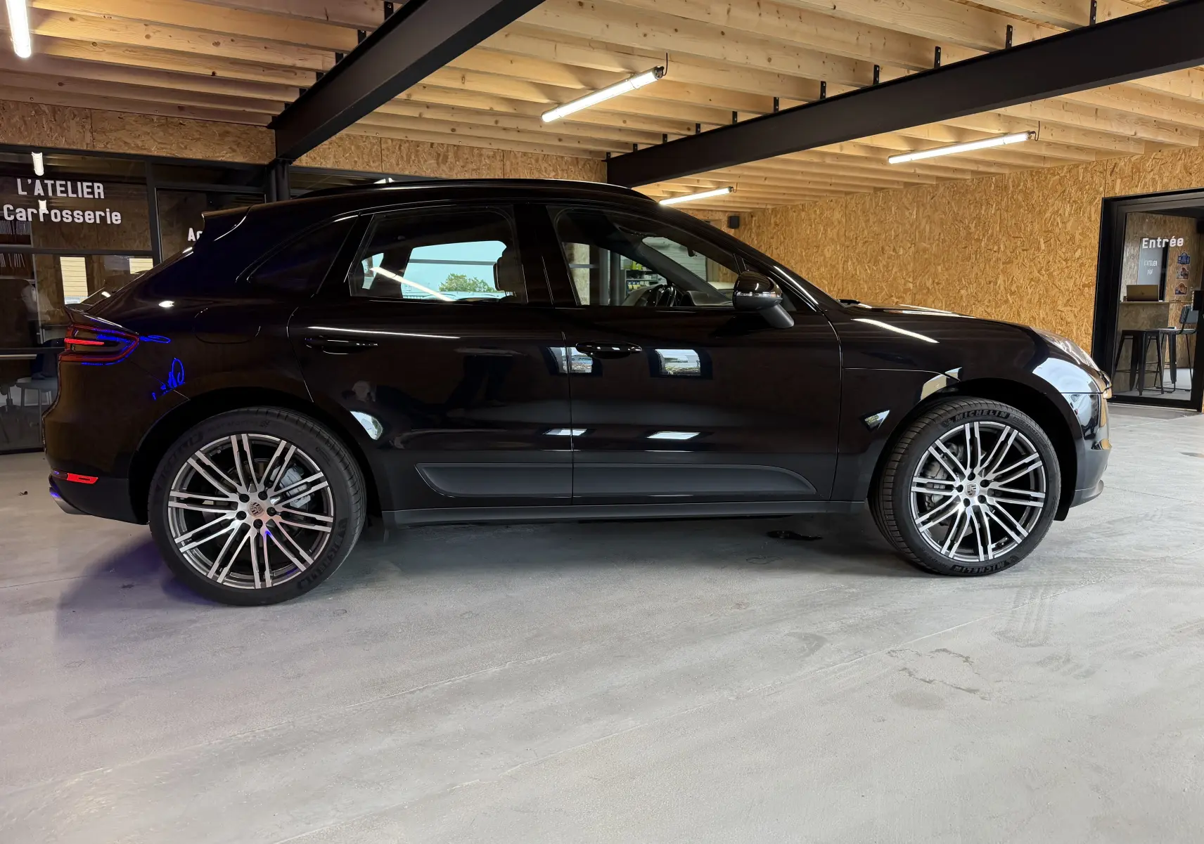 Vue de profil côté gauche d'un Porsche Macan S noir avec jantes alu 21 pouces dans un garage.