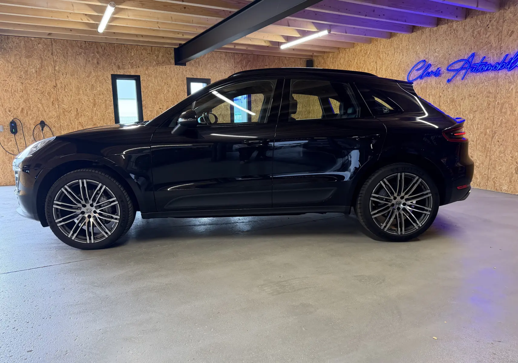 Vue de profil côté gauche d'un Porsche Macan S noir avec jantes alu 21 pouces dans un garage.