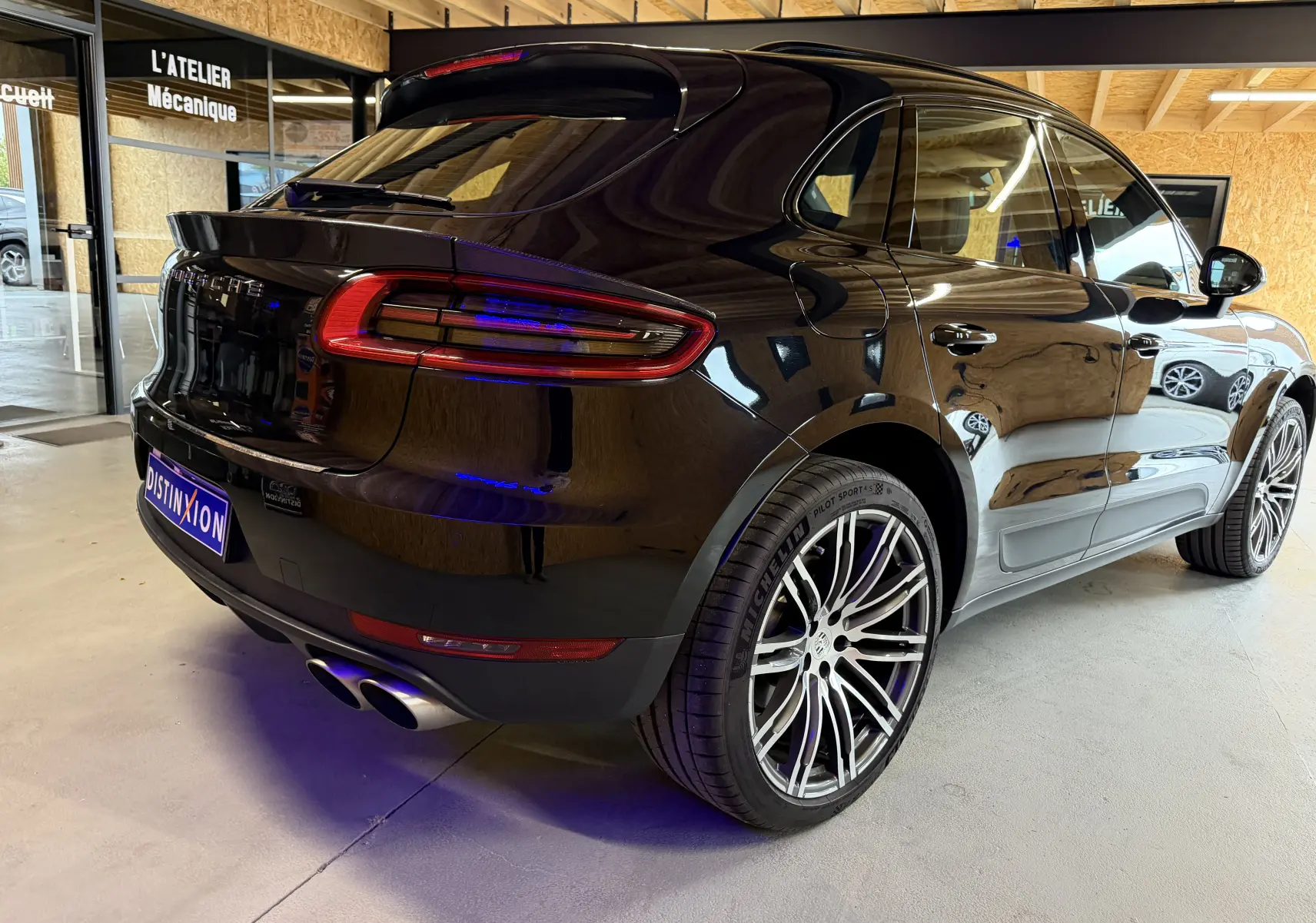 Vue 3/4 arrière droite d'un Porsche Macan S noir brillant avec jantes alu 21 pouces et doubles sorties d'échappement sport.