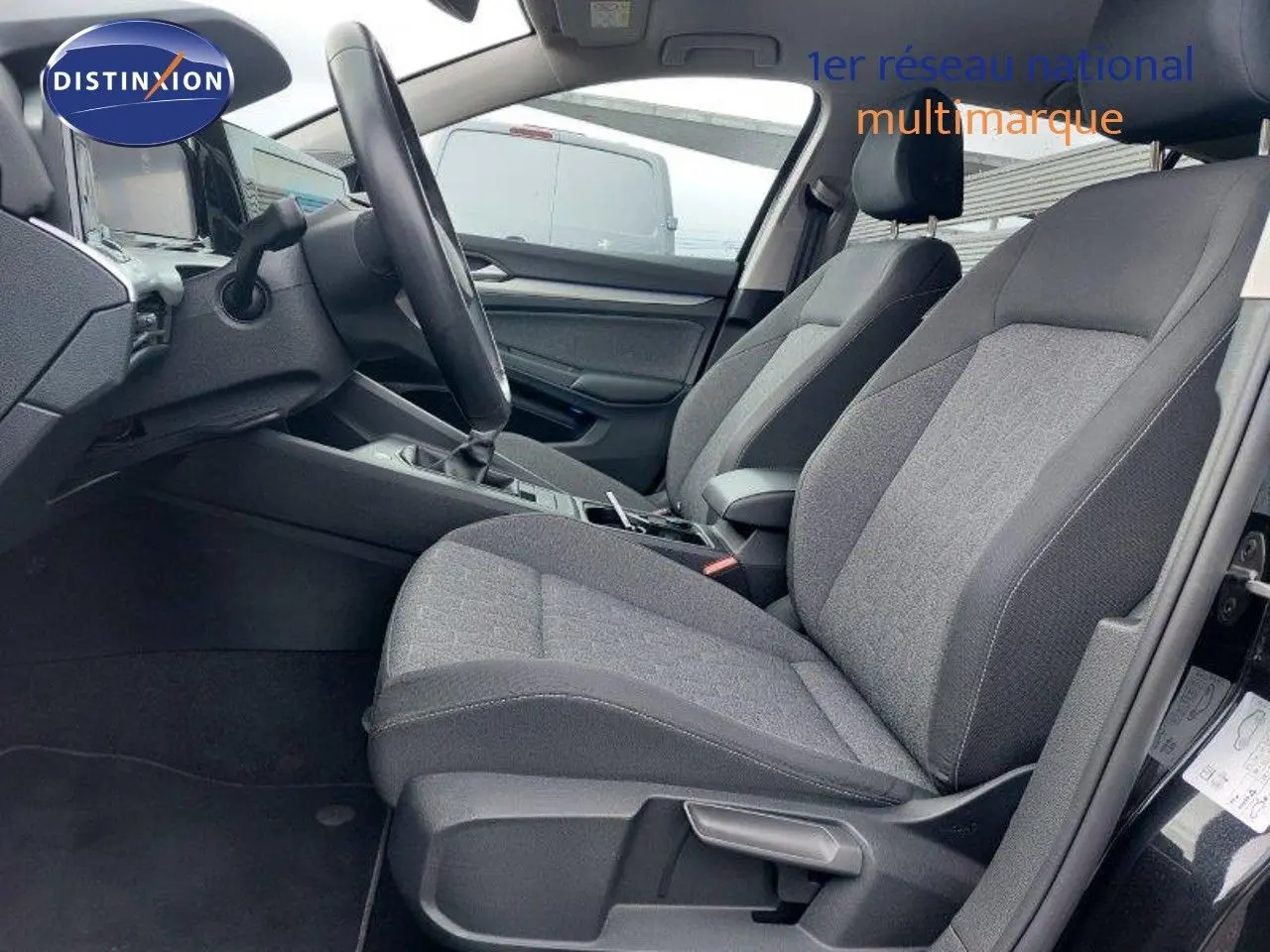 Vue intérieure côté conducteur d'une Volkswagen Golf 1.5 TSI noire, montrant les sièges tissu gris et la console centrale.