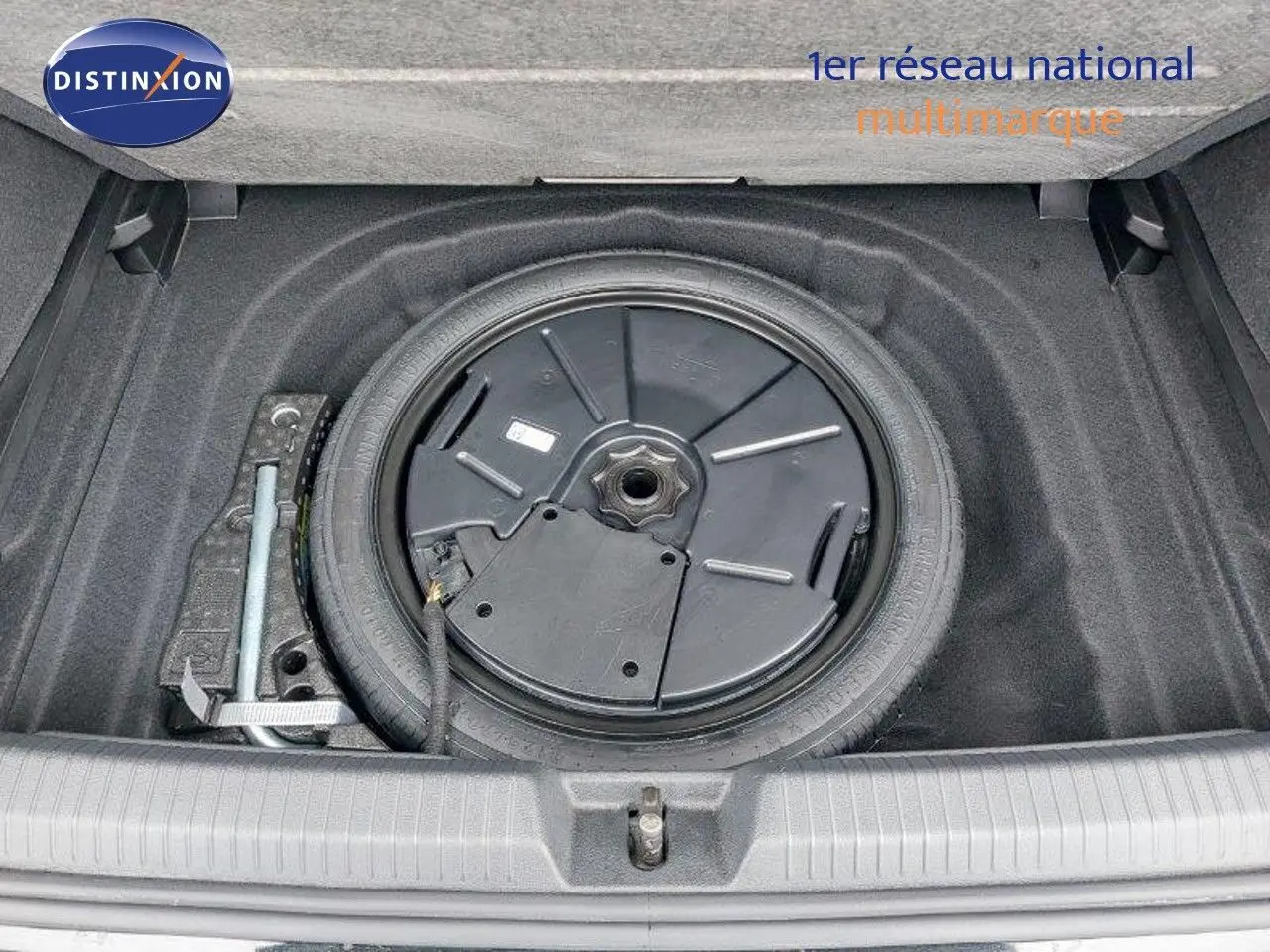 Vue plongeante sur la roue de secours et le compartiment de rangement dans le coffre d'une Volkswagen Golf noire 2024.
