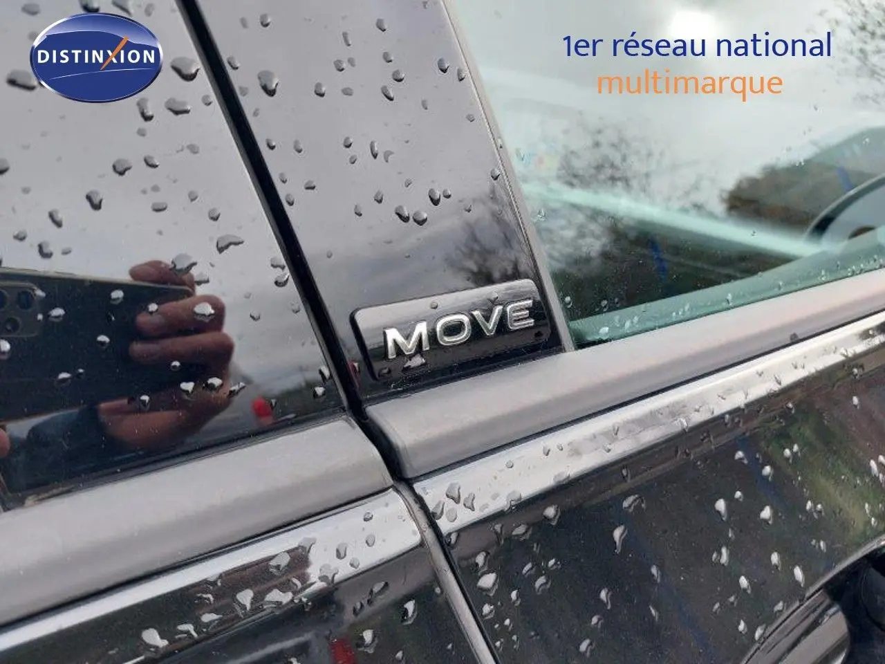 Gros plan sur l’inscription MOVE sur la portière arrière côté gauche d’une Volkswagen Golf noire métallisée sous la pluie.