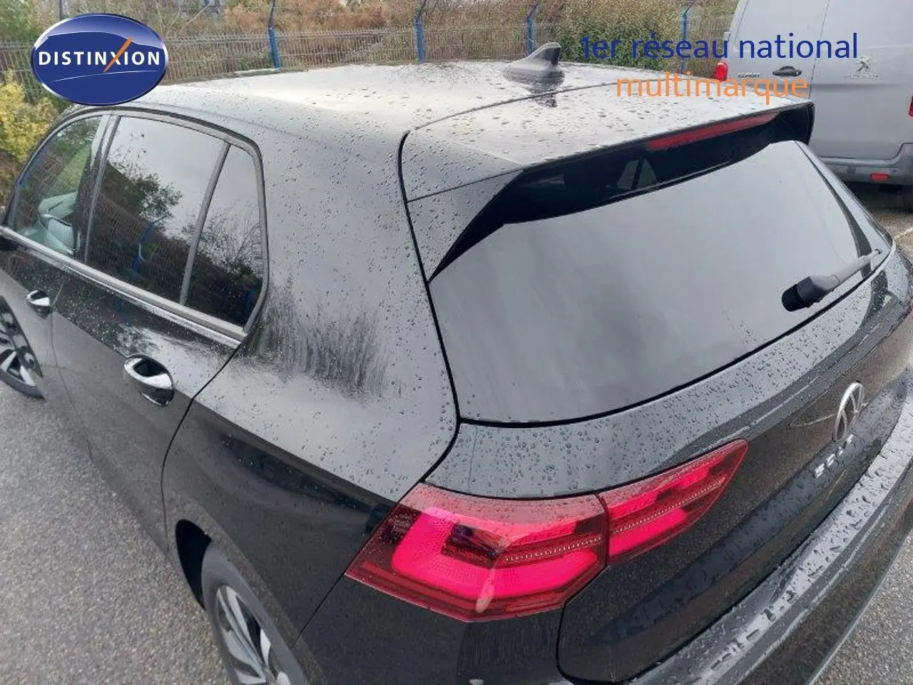 Vue 3/4 arrière droite d'une Volkswagen Golf noire métal 2024 avec feux arrière allumés sous la pluie.