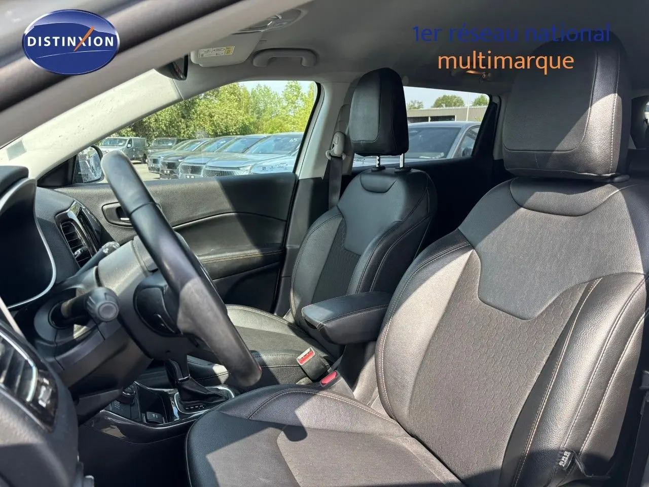 Vue intérieure côté conducteur du Jeep Compass 2021 blanc, sièges en cuir noir avec accoudoir central et tableau de bord visible.