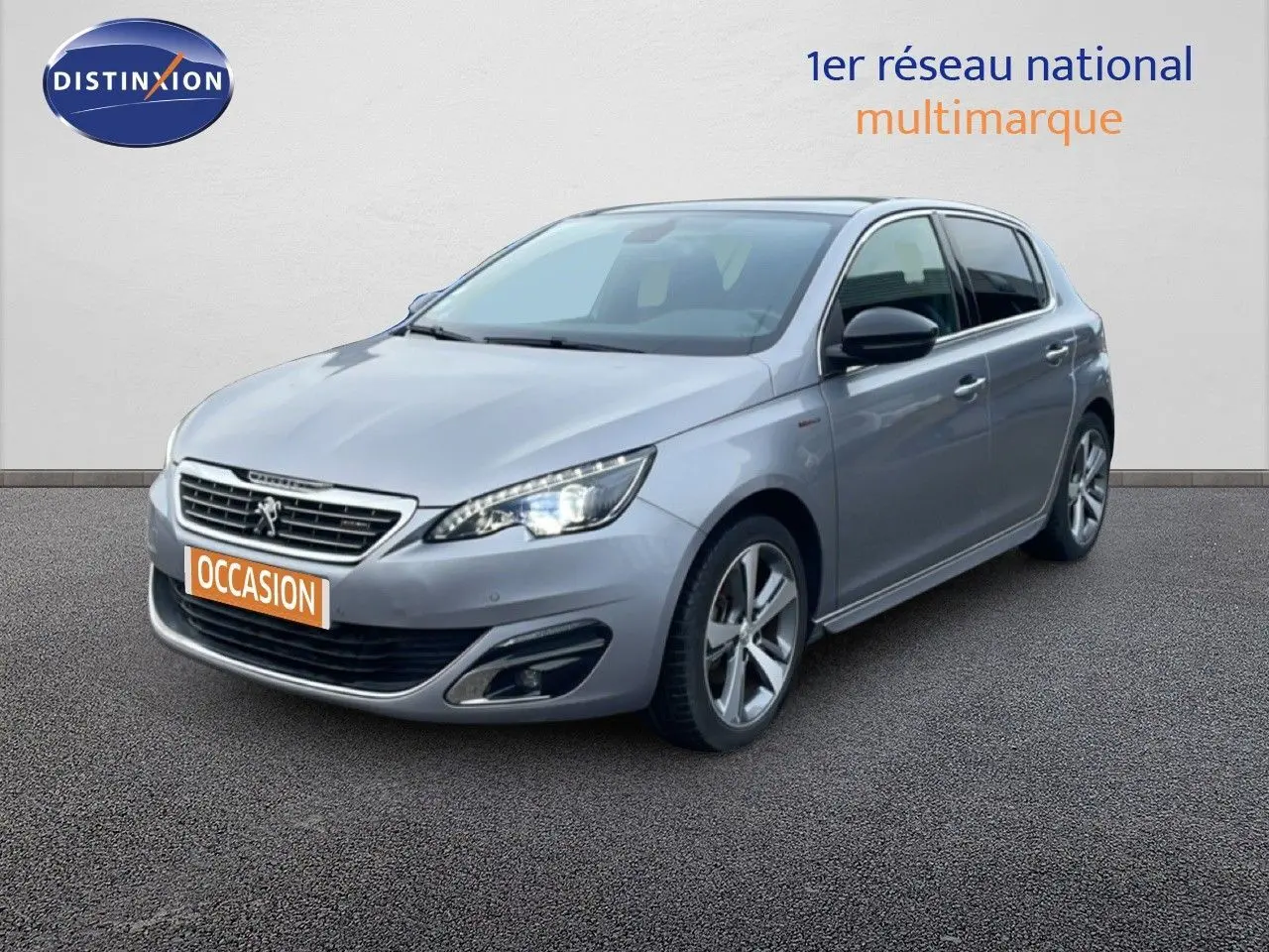 Peugeot 308 gris Artense vue 3/4 avant droit, avec phares allumés et jantes alliage distinctives.