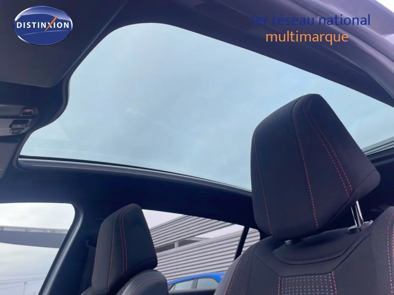 Vue intérieure sur les sièges avant noirs avec surpiqûres rouges et toit panoramique ouvert d'une Peugeot 308 gris Artense.