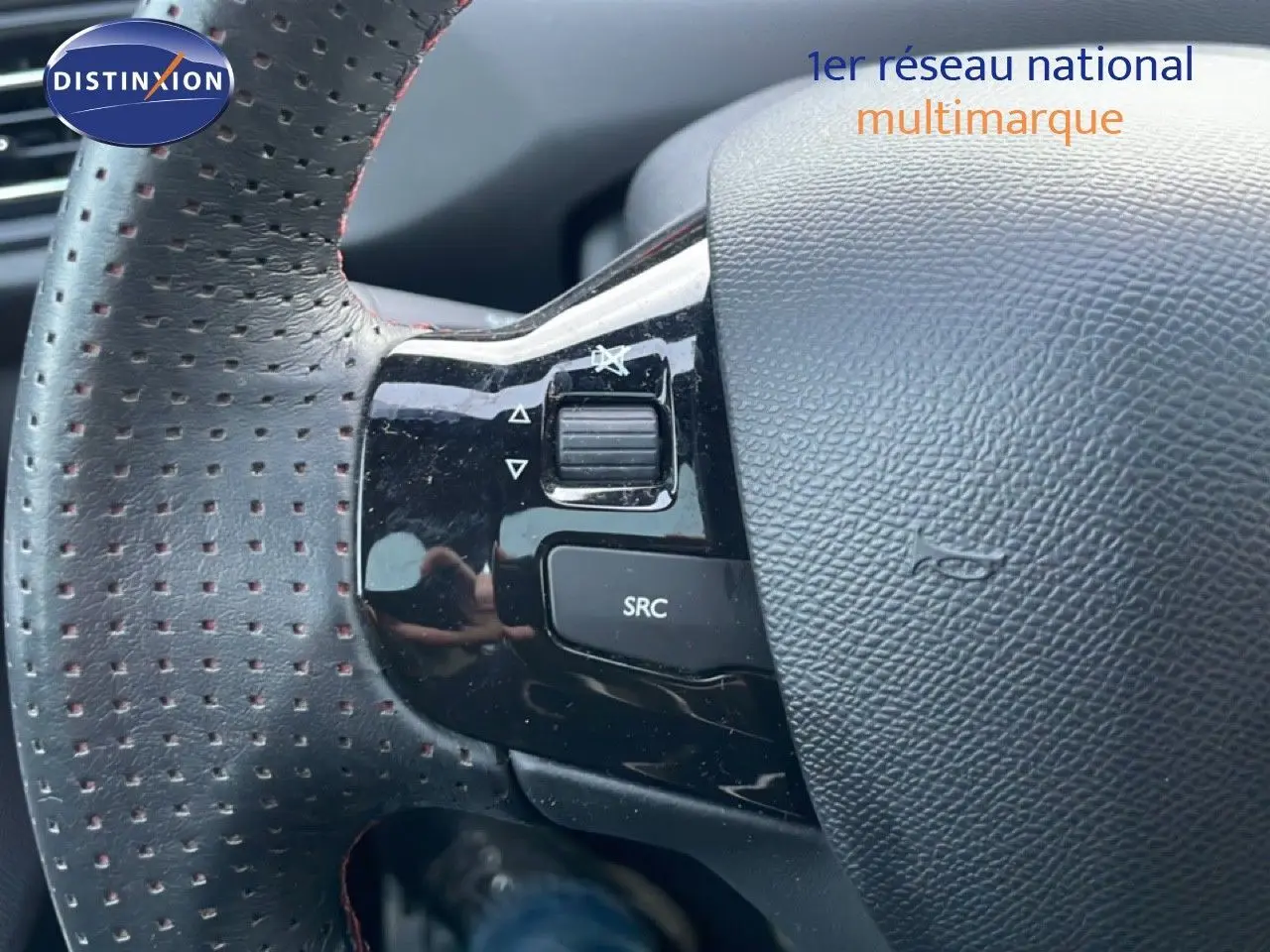 Gros plan sur la partie gauche du volant perforé noir de la Peugeot 308 gris Artense avec commandes audio intégrées.