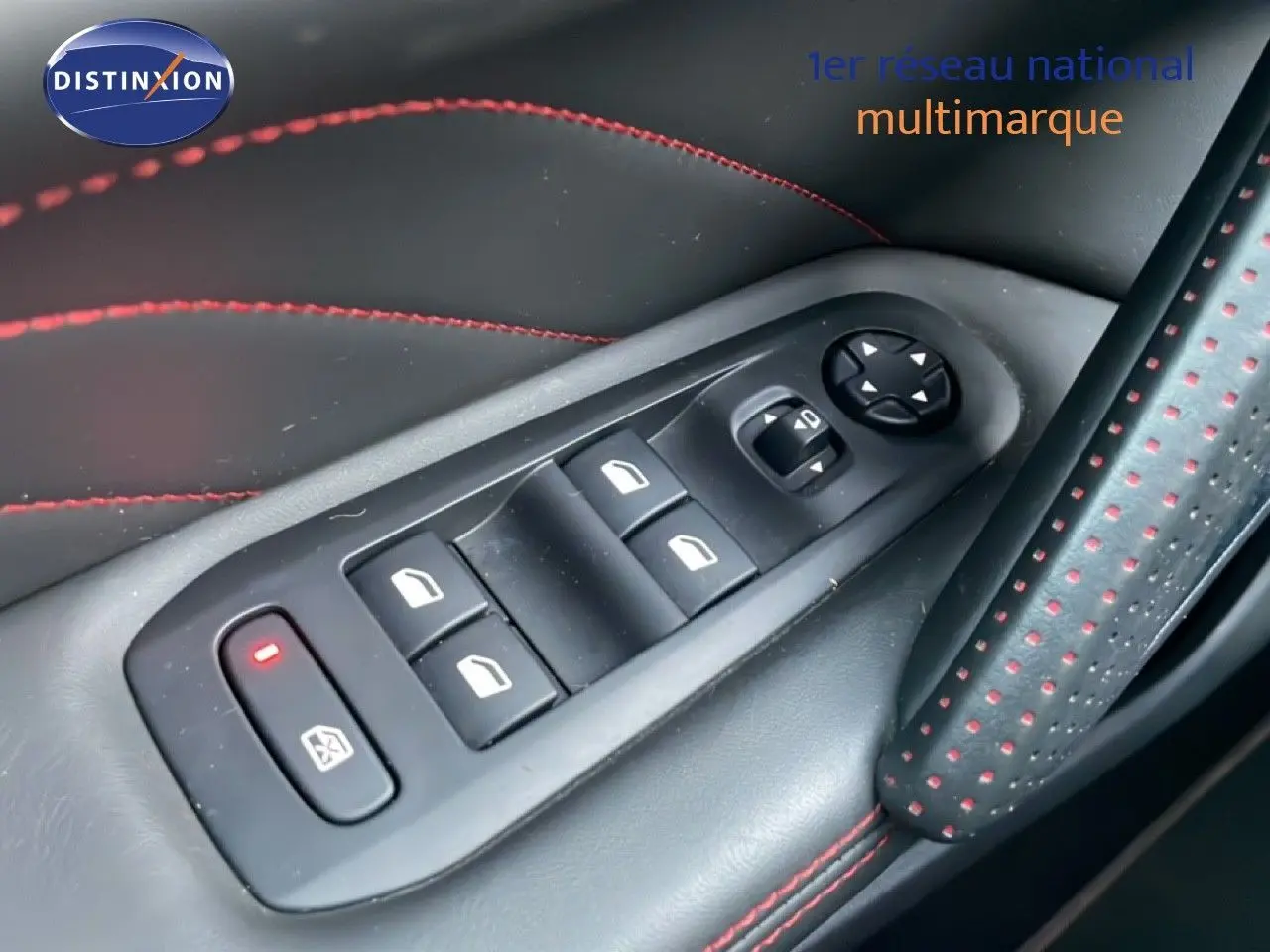 Gros plan sur les commandes de lève-vitres et réglages des rétroviseurs sur la porte côté gauche avec surpiqûres rouges.