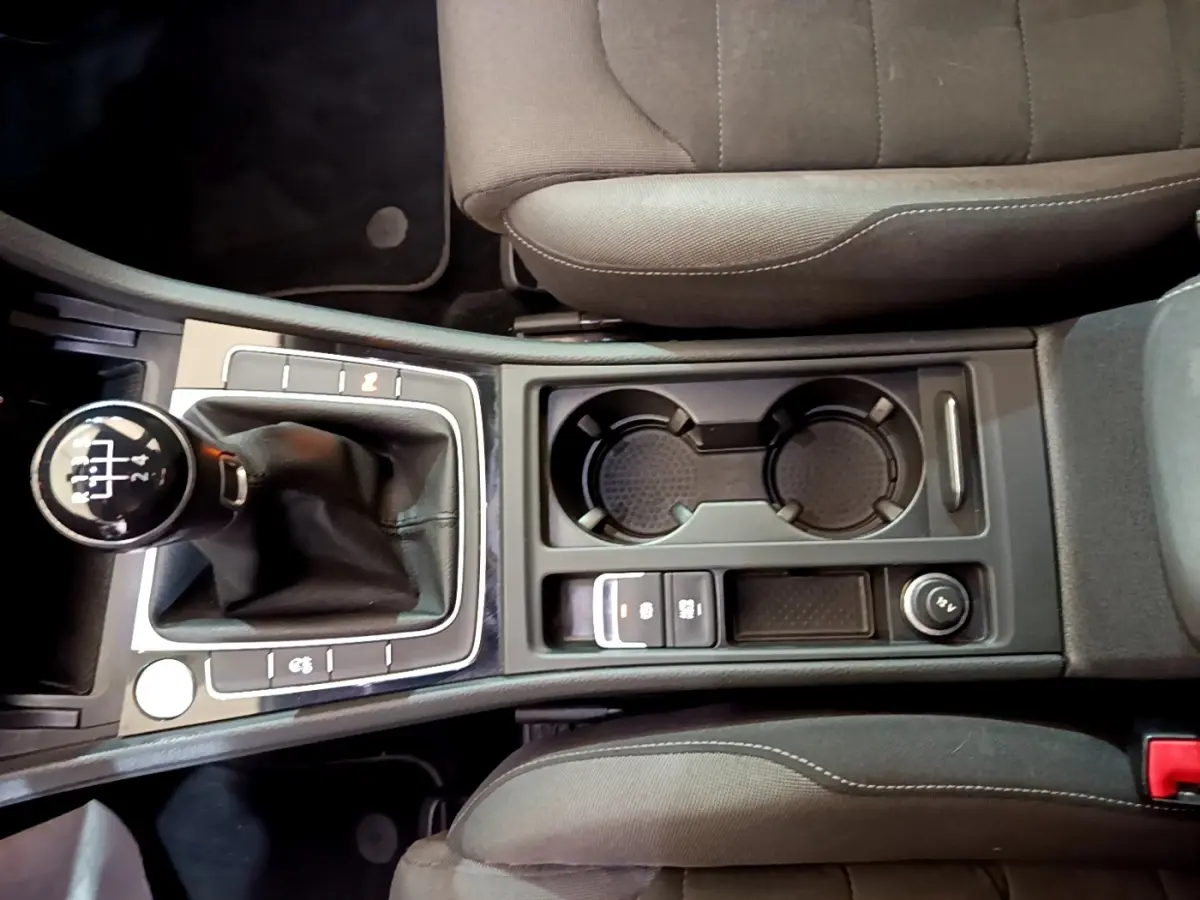 Vue plongeante sur la console centrale de la Volkswagen Golf gris clair, montrant levier de vitesse manuel et porte-gobelets.