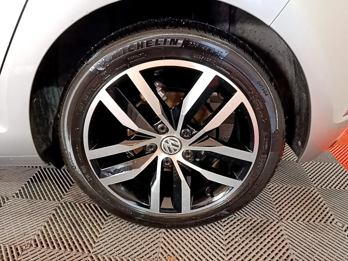 Gros plan sur la jante alliage bicolore noir et argent d'une Volkswagen Golf gris clair, roue avant droite visible.