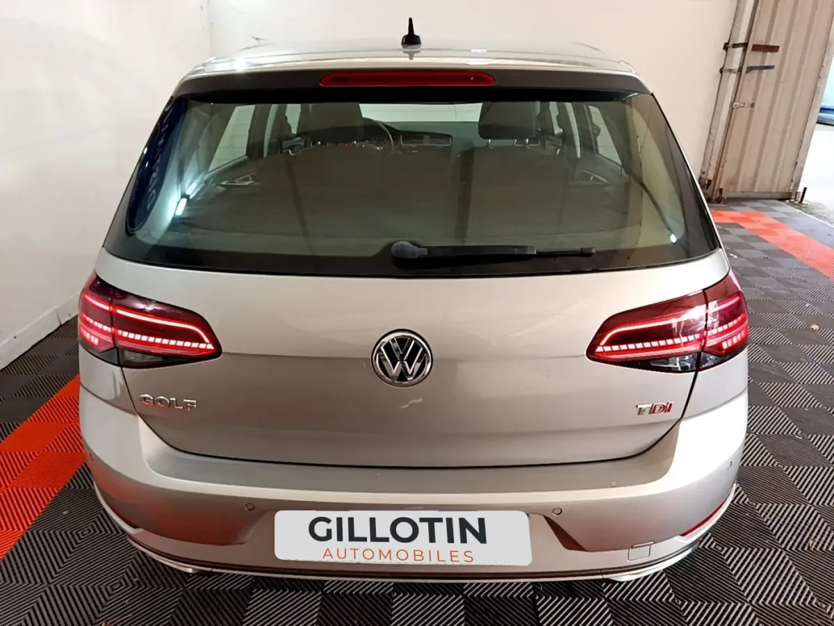 Vue arrière d'une Volkswagen Golf gris clair avec feux LED allumés dans un garage.