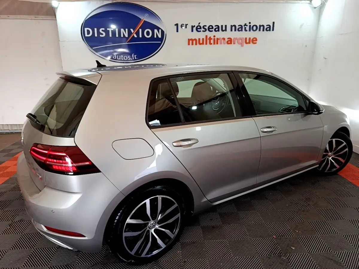 Vue 3/4 arrière droite d'une Volkswagen Golf gris clair 2017 avec jantes alliage et feux arrière LED allumés.