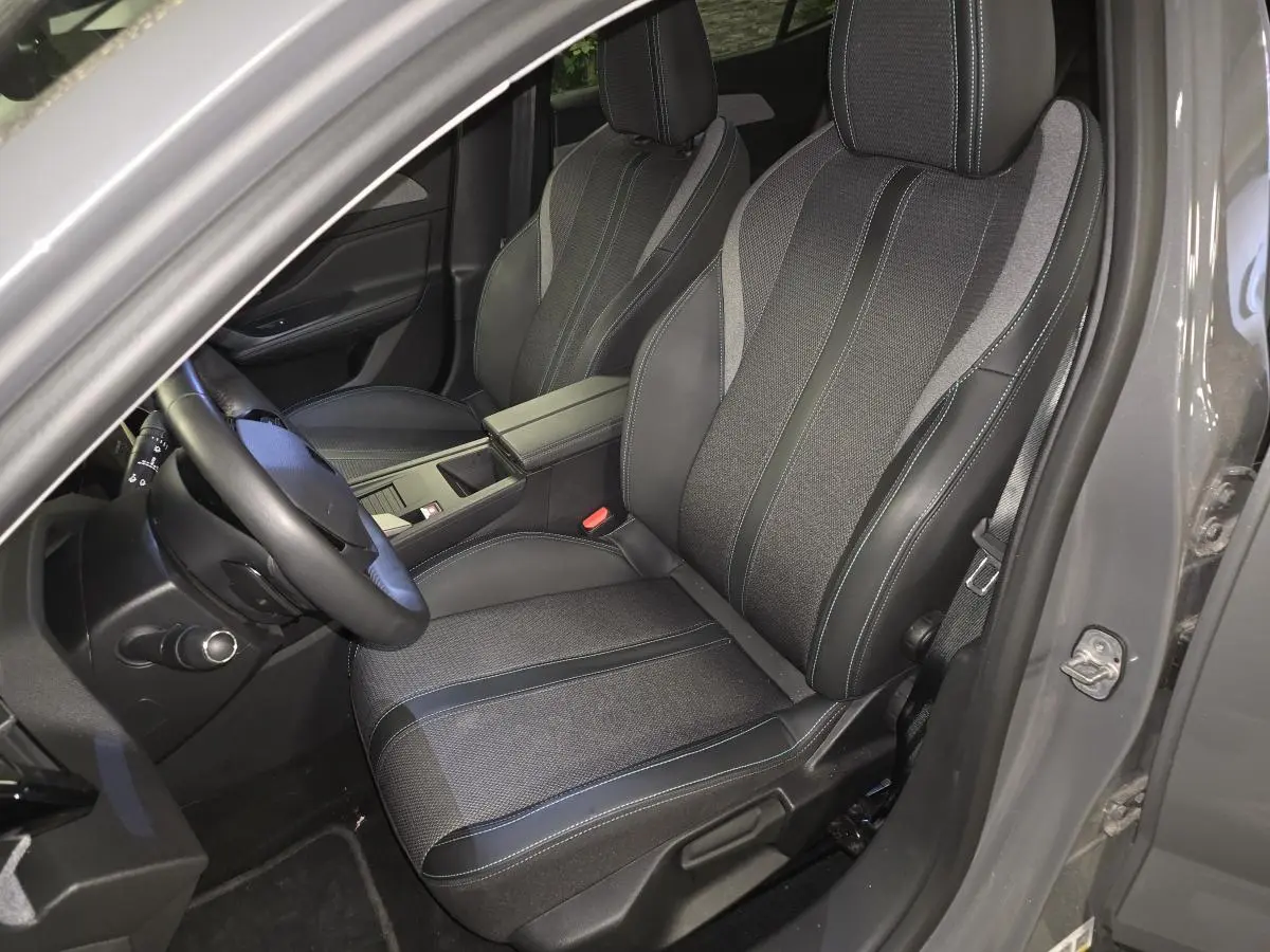 Vue intérieure côté conducteur de la Peugeot 408 gris, sièges tissu et cuir avec surpiqûres bleues et accoudoir central.