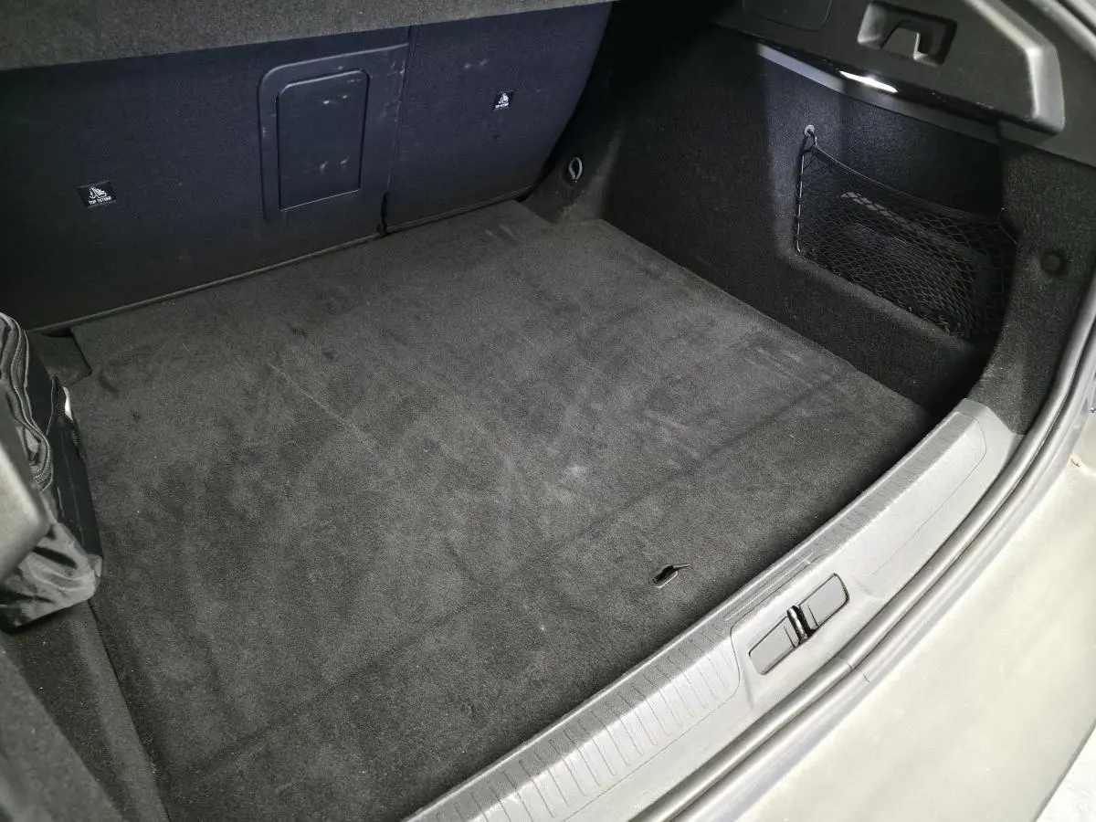 Vue rapprochée de la partie arrière du coffre gris du Peugeot 408 1.2i Hybrid avec tapis noir et filet de rangement latéral.