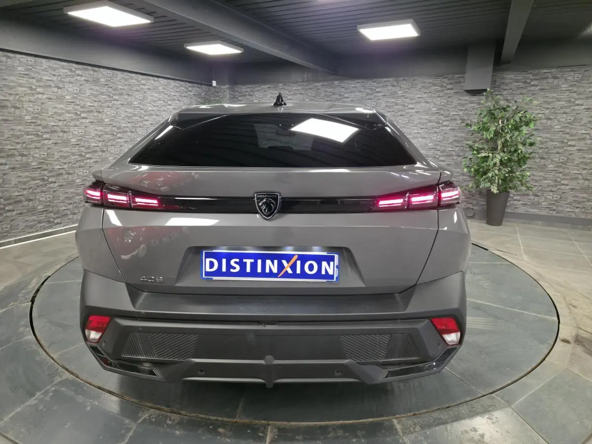 Vue arrière d'une Peugeot 408 gris métallisé avec feux LED allumés et logo lion central sur fond noir brillant.