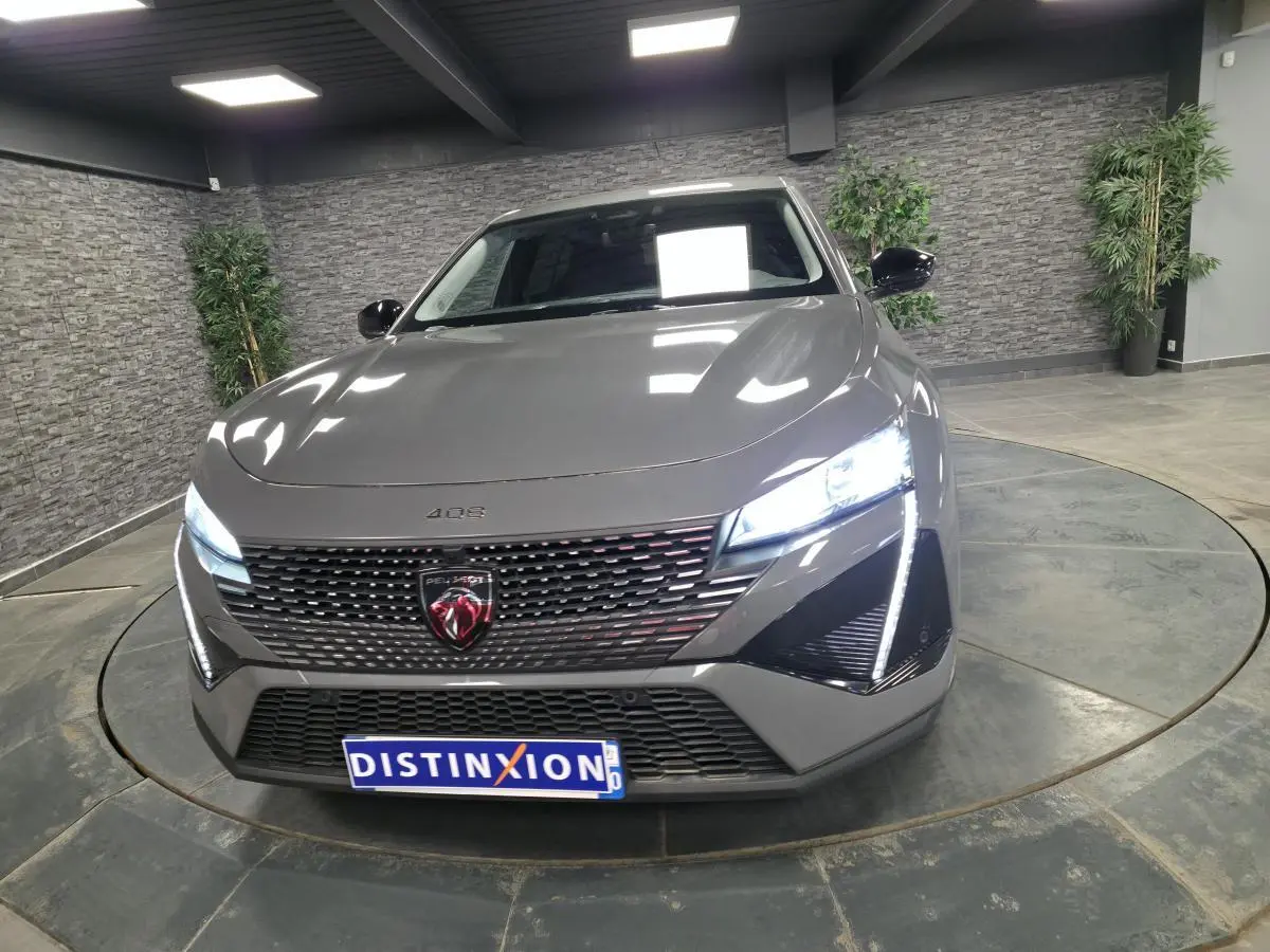 Vue avant d'une Peugeot 408 gris métallisé avec calandre noire et feux LED allumés dans un showroom.