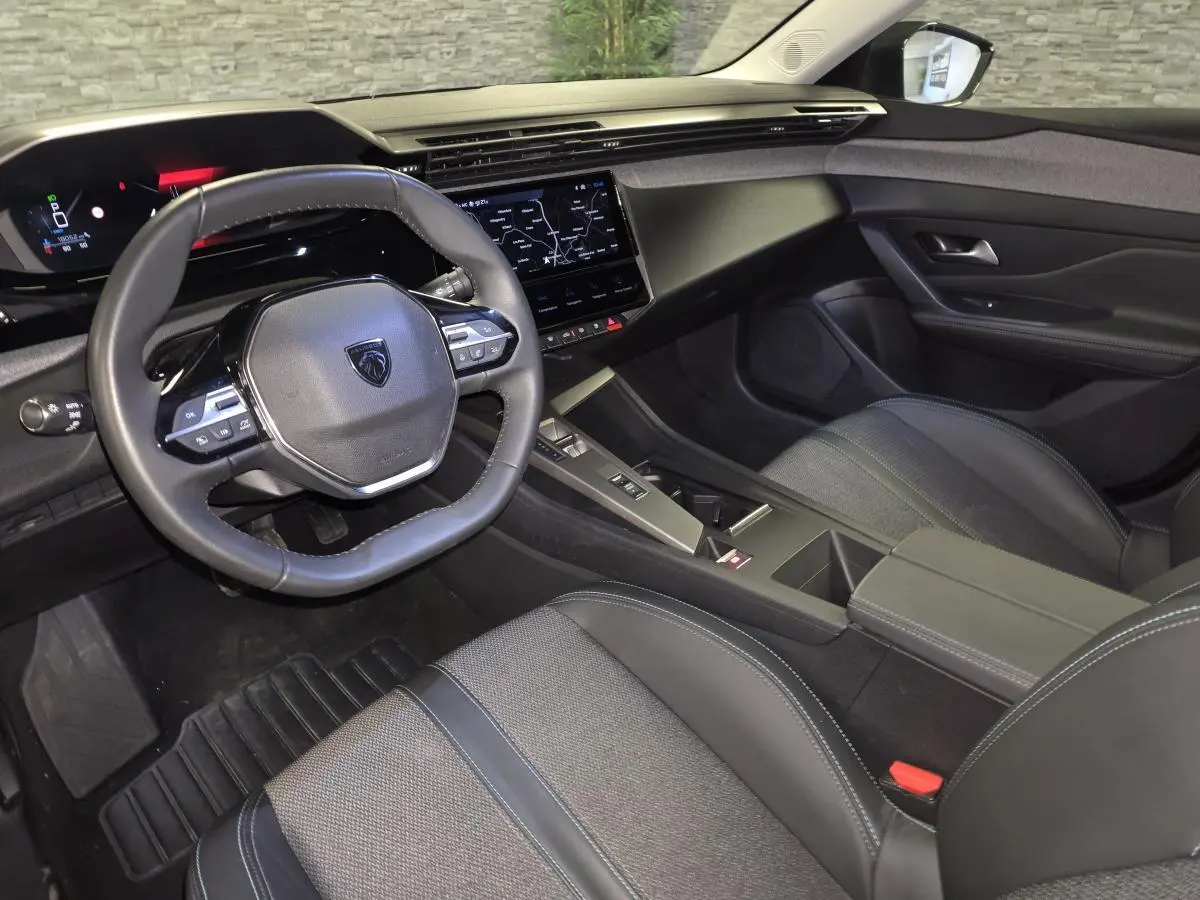 Vue intérieure côté conducteur du Peugeot 408 2025, avec tableau de bord numérique et sellerie tissu gris foncé.
