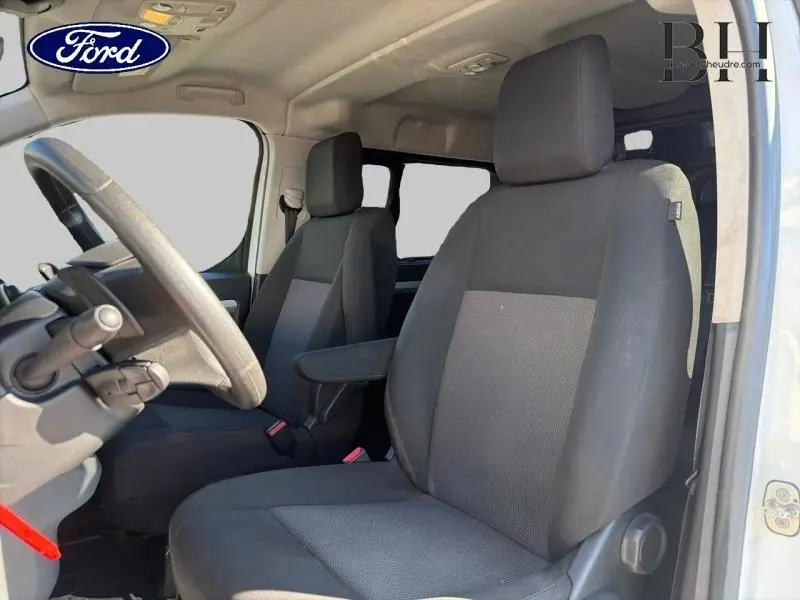 Vue intérieure côté conducteur du Citroën Jumpy blanc Banquise, sièges tissu gris avec accoudoir central.