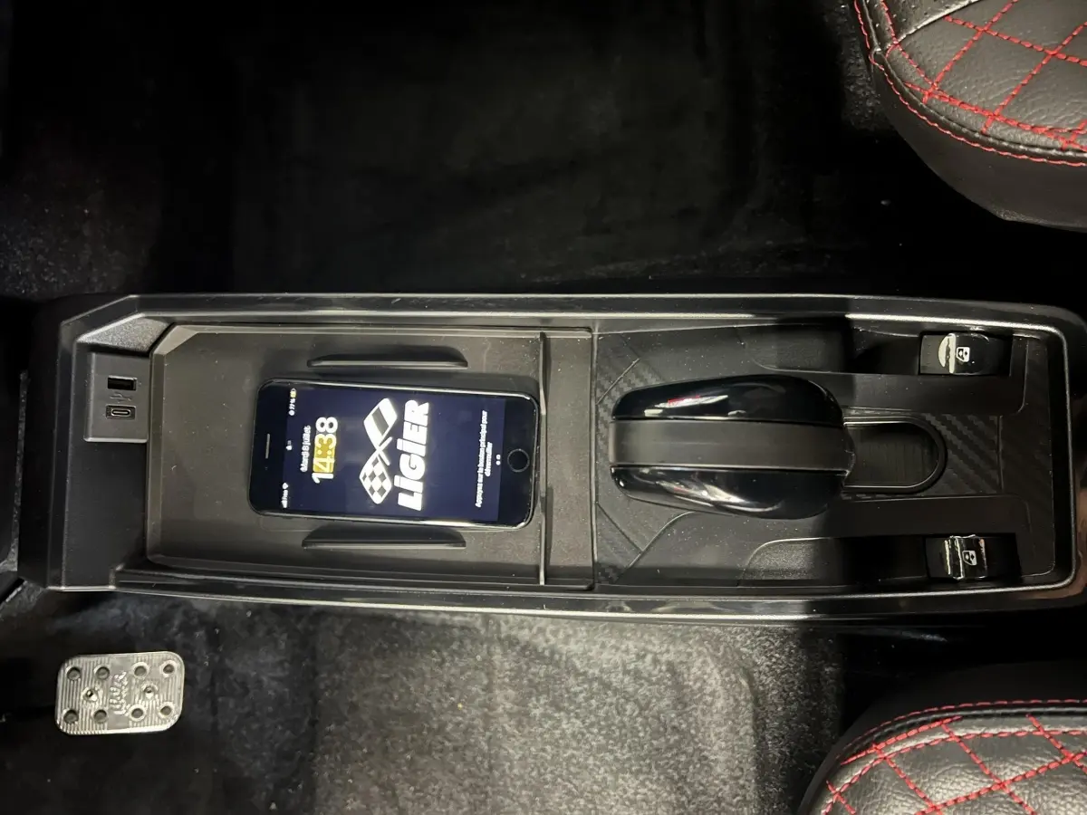 Vue plongeante sur la console centrale noire du Ligier JS50 bleu, avec levier de vitesses et smartphone posé dessus.