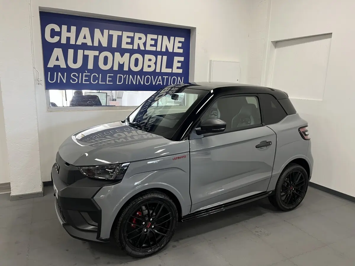 Vue 3/4 avant droite d'une Ligier JS50 grise avec toit noir et jantes noires en showroom.