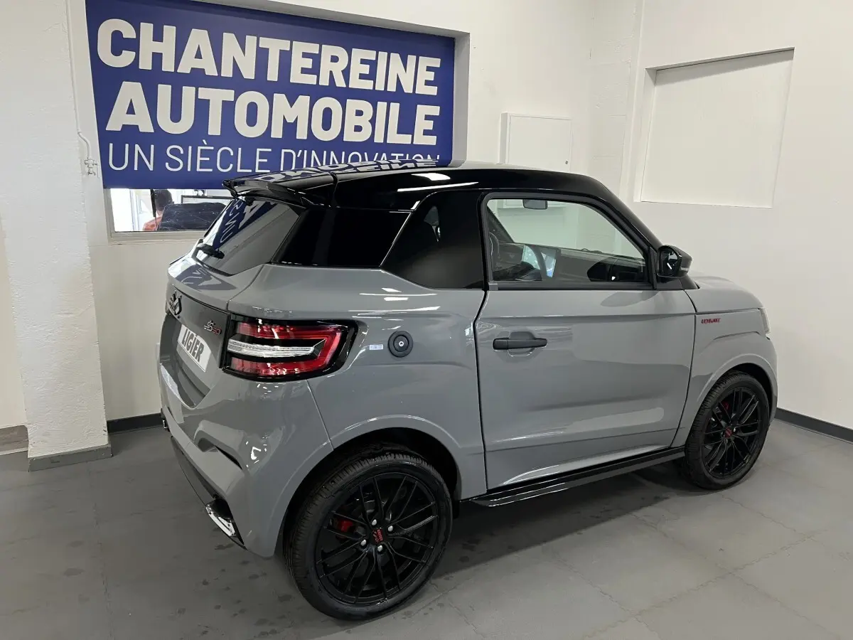 Vue 3/4 arrière droite de la LIGIER JS50 0.5 REVO D+ ULTIMATE grise avec toit noir et jantes noires en intérieur showroom.