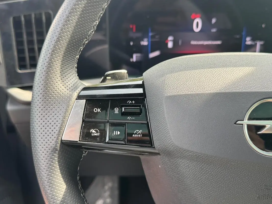 Gros plan sur le volant gris perforé de l’Opel Astra 2024 avec commandes multifonctions à gauche et logo central.